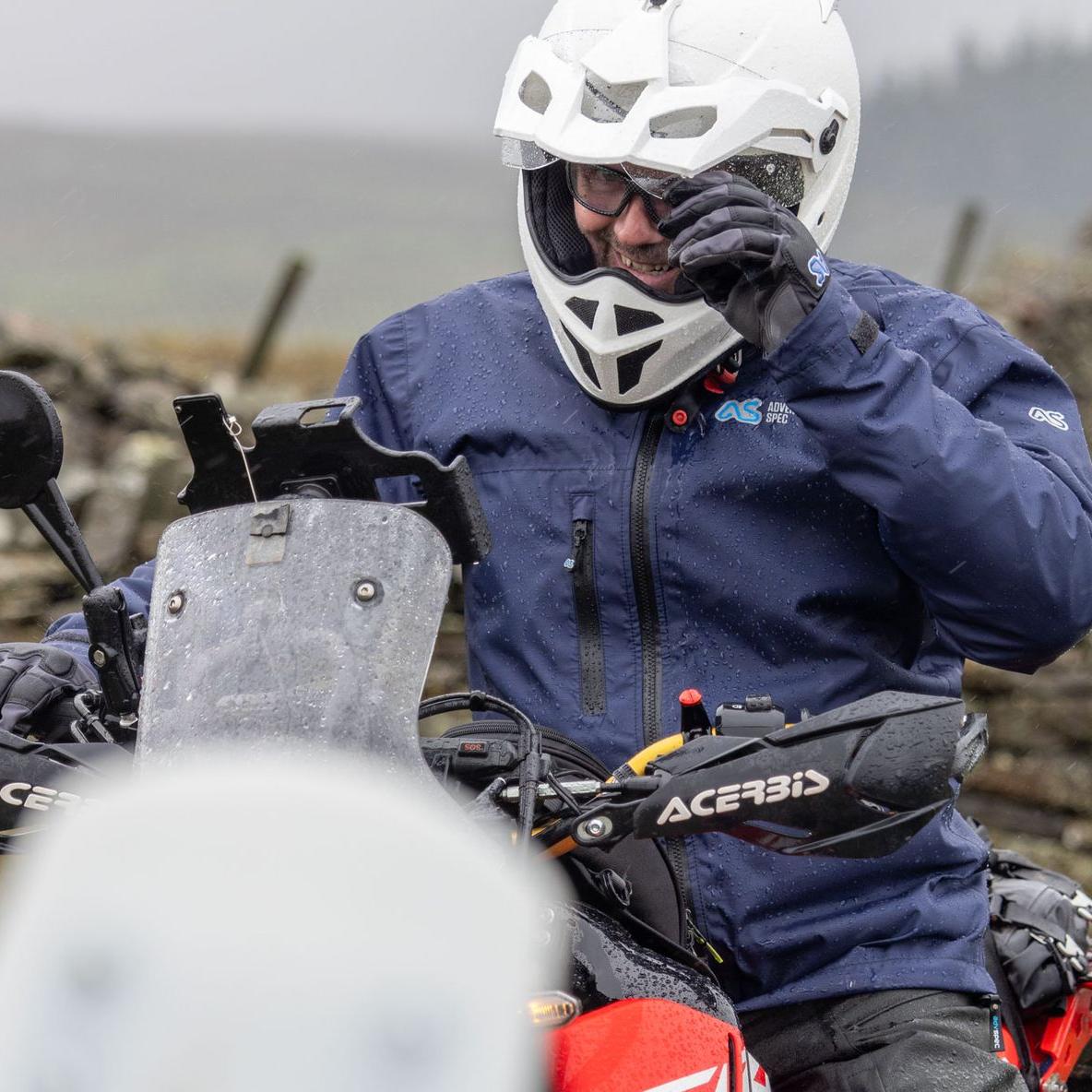 man wearing blue aqua pac jacket smiling at camera through open white helmet while it rains