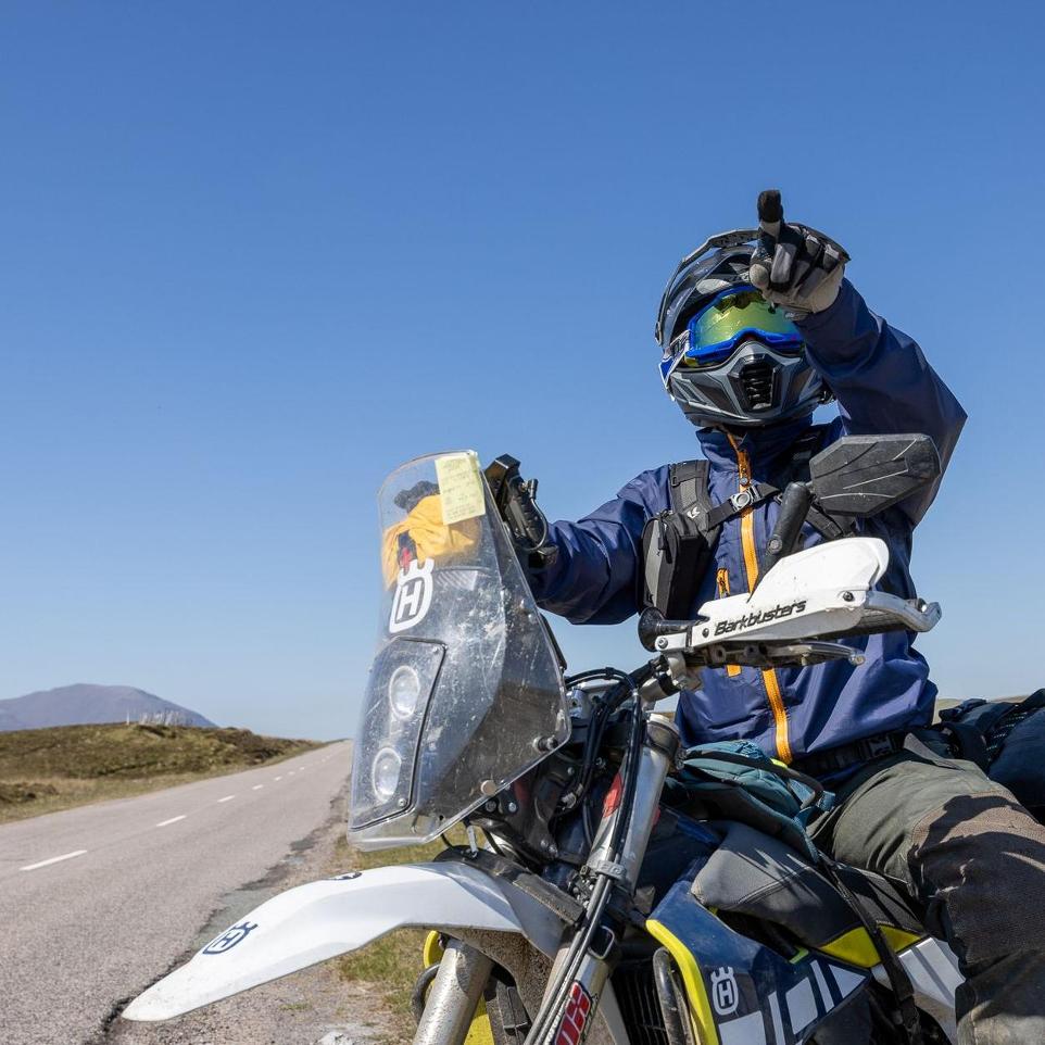 man pointing to the horizon on a husqvarna 701 motorbike with a big blue sky behind him